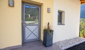 A modern entrance area with a gray front door and a large window. Next to the door stands a decorative planter.