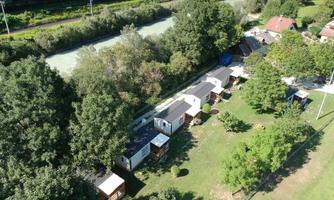 An aerial view of several holiday homes in a green landscape. In the background, a calm river flows, surrounded by trees.