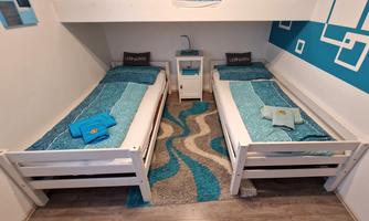 A cozy room with two single beds and blue-white decoration. There is a small table and a rug with wave-patterned design.