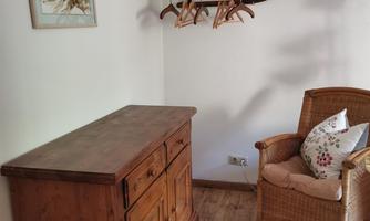 A cozy room with a wooden wardrobe and a rattan chair. On the wall hangs a coat rack with wooden hangers.
