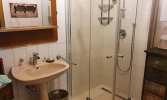 A bathroom with a glass shower and a sink. On the wall, there is a mirror and a wooden shelf.