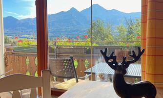 A cozy table with a small plastic antler stands in the foreground. In the background, there is a beautiful view of the mountains and a blue sky.