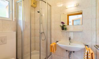 A modern bathroom with a shower cabin and a sink. Orange towels are hanging on the wall and a plant is standing on the shelf.