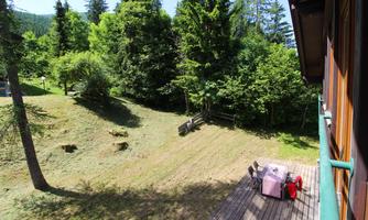 A peaceful landscape with a wooden terrace and plenty of green forest. In the foreground, there is a table and chairs for relaxing.