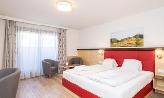 A modern hotel room with two beds, a table, and two armchairs. Large windows provide plenty of daylight and a cozy atmosphere.