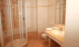 A modern bathroom with a shower, sink, and toilet. The walls are tiled in a light color and the floor has a warm tone.
