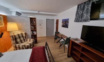 A cozy room with a bed, an armchair, and a table. The walls are in light shades, and there is pleasant lighting.