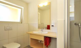 A modern bathroom with a shower, a sink, and a toilet. It is bright and minimally furnished.