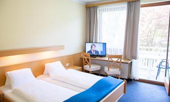 A simple hotel room with two beds and a blue throw. There is a television and access to a balcony through the windows.