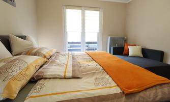 A cozy bedroom with a double bed and an additional sofa bed. Large windows let in plenty of light and the room is designed in warm colors.