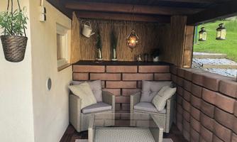 A cozy seating area with two chairs and a table. Surrounded by a rustic façade and decorative plants.