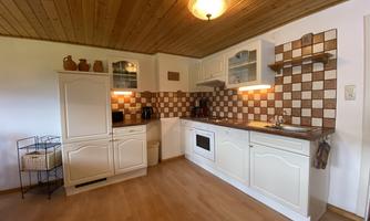 A modern kitchen with white furniture and a wooden ceiling. The walls are decorated with a checkered tile design.