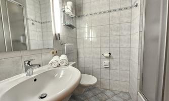 A modern bathroom with tiles and a sink. Towels are neatly arranged, and a shower is available.