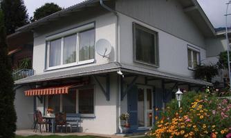 A beautiful house with a well-kept garden and colorful flowers. On the terrace, there are furniture and an umbrella for relaxation.