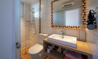 A modern bathroom with a shower and a sink on a wooden table. The walls are brightly tiled and decorated with colorful accents.