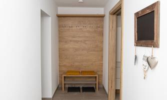 A bright hallway with white walls and a wooden panel. In the middle, there is a bench and a small board is hanging on the wall.