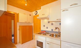 A small, modern kitchen with a wooden ceiling and bright cabinets. The equipment includes a stove, a sink, and space for kitchen utensils.