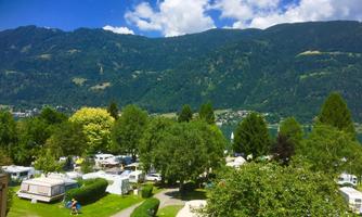 A beautiful campsite with many trees and RVs. Majestic mountains and a clear sky can be seen in the background.