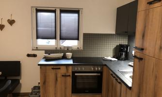 A modern kitchen with wooden cabinets and a dark work area. Windows with blinds provide ample light.