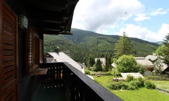 A beautiful view from a balcony of green mountains and a quiet village. The sky is partly cloudy with occasional blue spots.