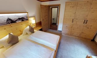 A cozy bedroom with two beds and modern wooden furniture. Through the door, a bathroom is visible.