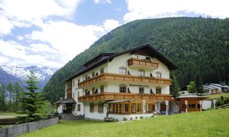 A charming house in the midst of nature, surrounded by green mountains. The building has several balconies and large windows that let in a lot of light.
