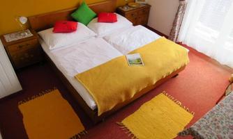 A cozy bedroom with two single beds and colorful cushions. The room has a warm hue and an inviting carpet.