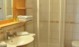 A modern bathroom with a shower cabin and a sink. There are towels on a shelf and a bright, friendly atmosphere.