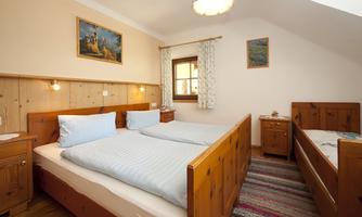A cozy bedroom with wooden furniture and two beds. There are windows with curtains and an artistically designed ceiling.