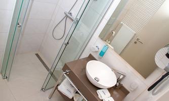 A modern bathroom with a glass enclosure and a large shower. Towels and care products are on the sink.