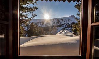 A view from a window of snow-covered mountains and the sun shining in the sky. The snow gently lies on the landscape.
