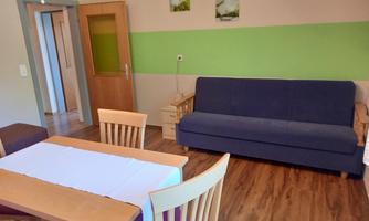 A cozy room with a blue sofa and a wooden table. Pictures hang on the walls, and the color scheme is in green and earth tones.