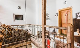 A rustic staircase with wooden balustrade and visible wooden beams. The room is bright and friendly, with some decorations and open windows.