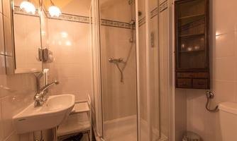 A small bathroom with a shower cubicle, a sink, and a toilet. The walls are tiled and the lighting is warm.