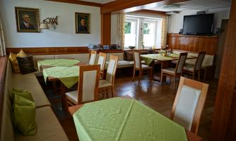 A cozy restaurant with wood paneling and bright tables. Portraits hang on the walls, and the windows let in plenty of light.