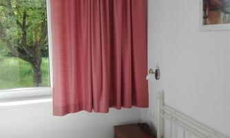 A cozy bedroom with a white bed and red curtains. Light streams through the window, creating an inviting atmosphere.