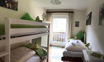 A bright room with a bunk bed and a single bed. The walls are decorated with a few pictures, and there is a balcony with a view.