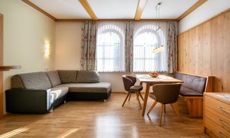 A modern living room with a cozy couch and a dining table. Large windows let in plenty of light, and the wooden paneling creates a warm atmosphere.