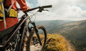 Ein Mountainbiker steht an einem Aussichtspunkt und schaut auf eine beeindruckende Landschaft. Hügel und Wälder erstrecken sich bis zum Horizont unter einem teilweise bewölkten Himmel.