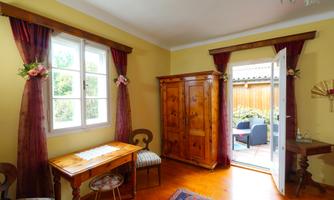 A cozy room with yellow walls and wooden details. A table stands next to a window, and the door opens to a lovely outdoor area.