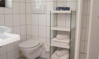 A modern bathroom with white tiles and a shower. Fresh towels are neatly stacked on a shelf.