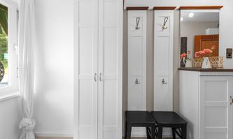 A bright entrance area with white furniture. Two black chairs are in front of a cabinet and hooks for coats on the wall.