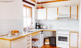 A bright and modern kitchen with white cabinets and wood details. It is well-equipped with various appliances and a small table.