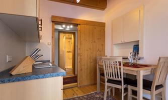 A cozy kitchen with wooden shelves and a dining table for four people. In the background, a bathroom with wood paneling can be seen.