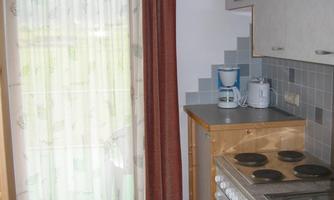 A small kitchen with wooden cabinets and modern appliances. A bright curtain hangs in front of the window.
