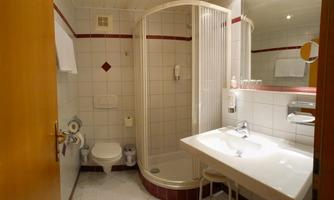 A modern bathroom with a shower cabin and a sink. The walls are tiled and there is bright lighting.