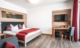 A modern bedroom with a large bed and wooden details. There is a television and a small workspace.