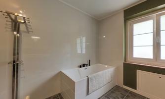 A modern bathroom with an elegant bathtub and a shower. Light gray tiles and a large window provide plenty of light.