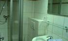 A small bathroom with a shower and a sink. The walls are tiled, and there is a mirror above the sink.