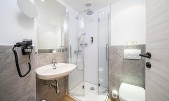A modern bathroom with a shower cabin, sink, and toilet. The walls are light, and the furnishings are contemporary.